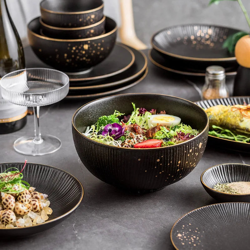 Set of black porcelain dinner plates with gilt rims, stylish ceramic tableware for serving food and salads in a modern kitchen.